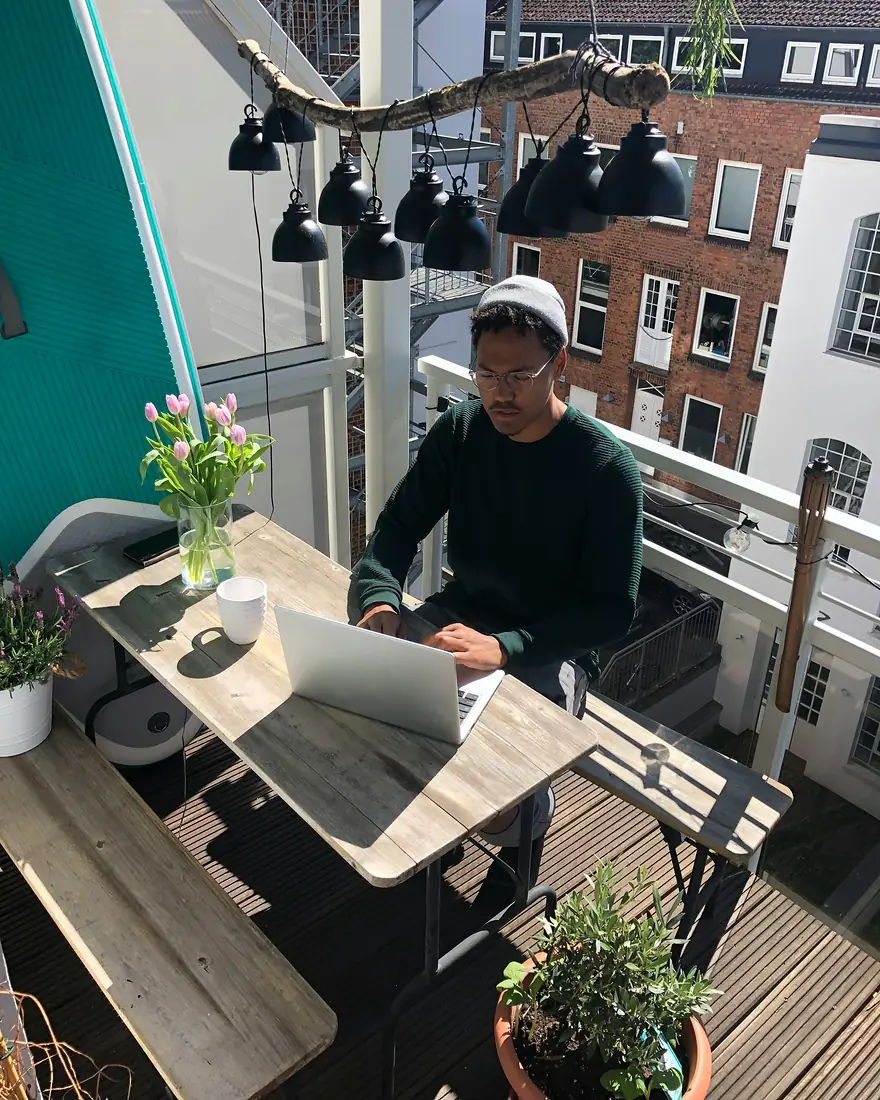 A founder working on his laptop on a Hamburg balcony, his phone face down beside him